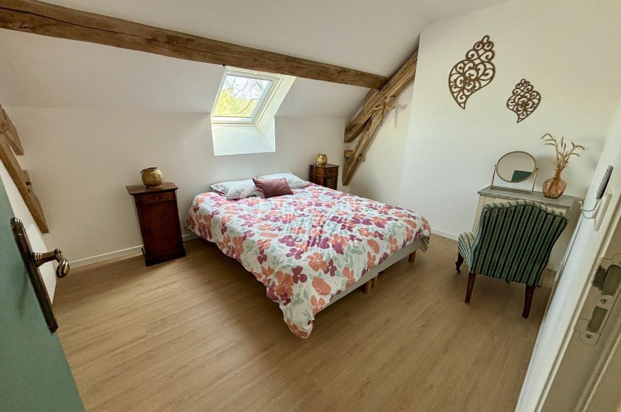Chambre mansardée avec lit double, poutres apparentes, mobilier en bois et chaise près d'un bureau.