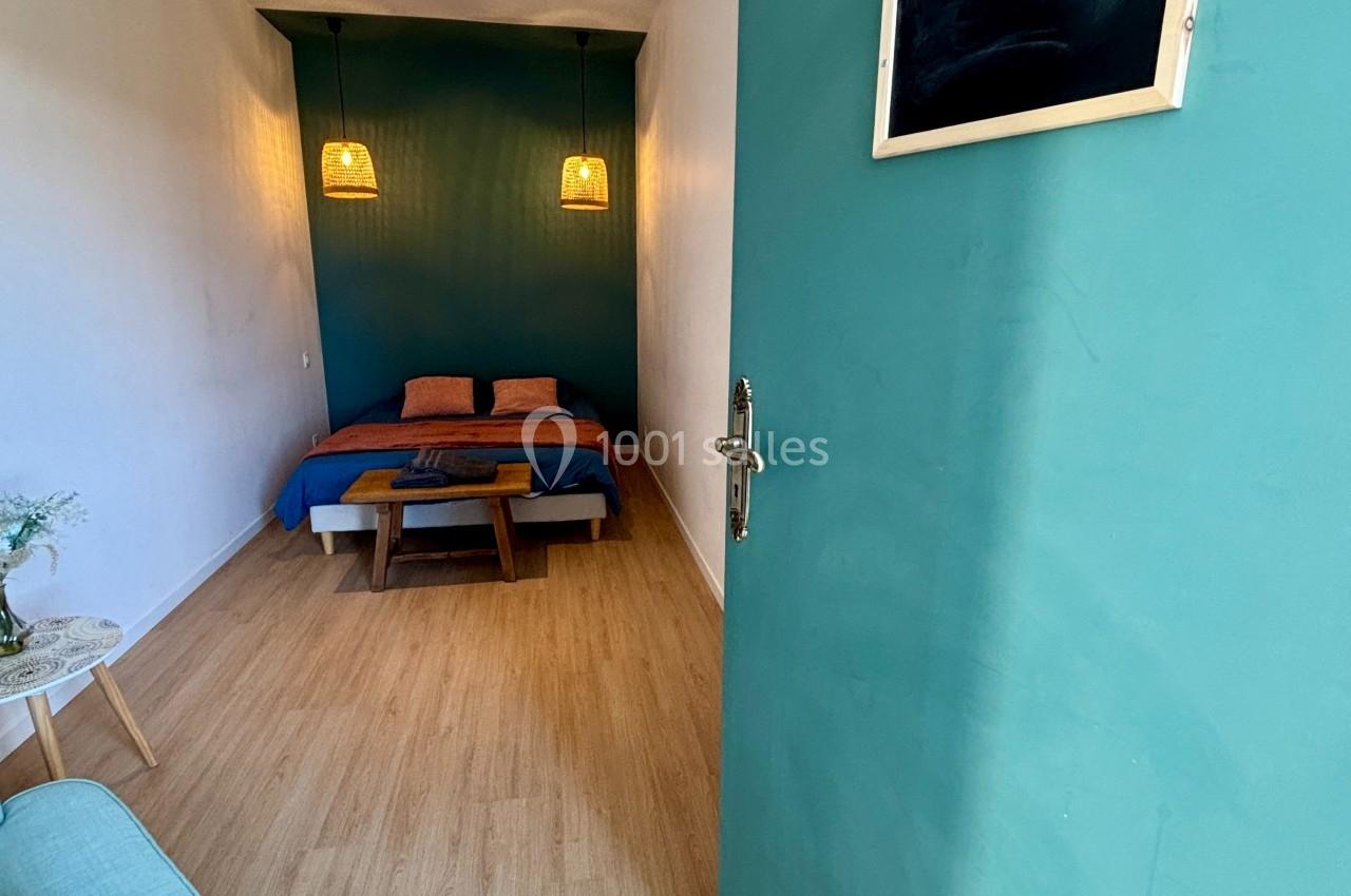 Vue d'une petite chambre avec un lit double, deux suspensions lumineuses et un sol en bois clair, prise depuis l'entrée.