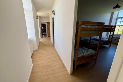 Miniature Au sein des gîtes : lieu de passage Ruines éclairées et bâtiment adjacent sous un ciel nocturne, avec un arbre illuminé et des bancs sur une pelouse.