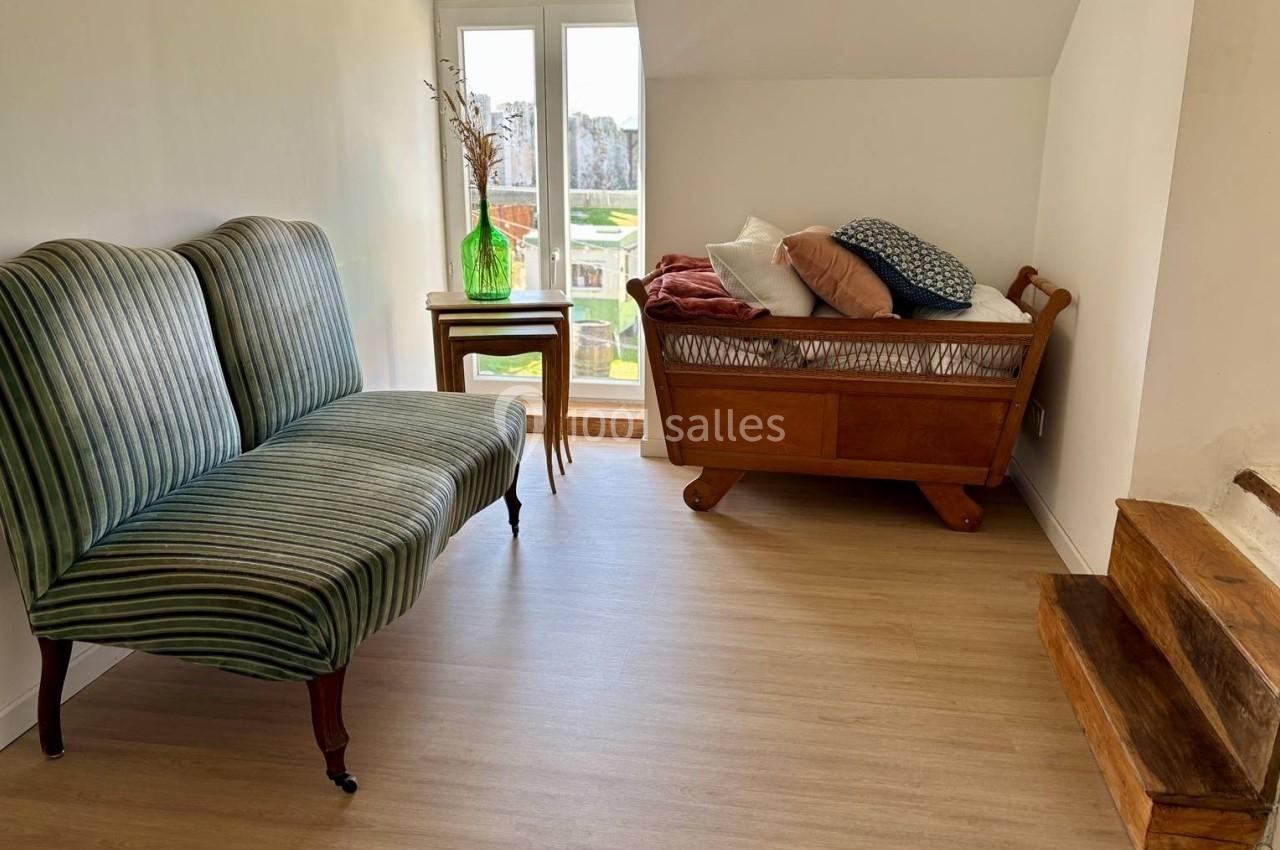 Petite pièce lumineuse avec un canapé rayé, un berceau en bois, une table et une vue sur un jardin.