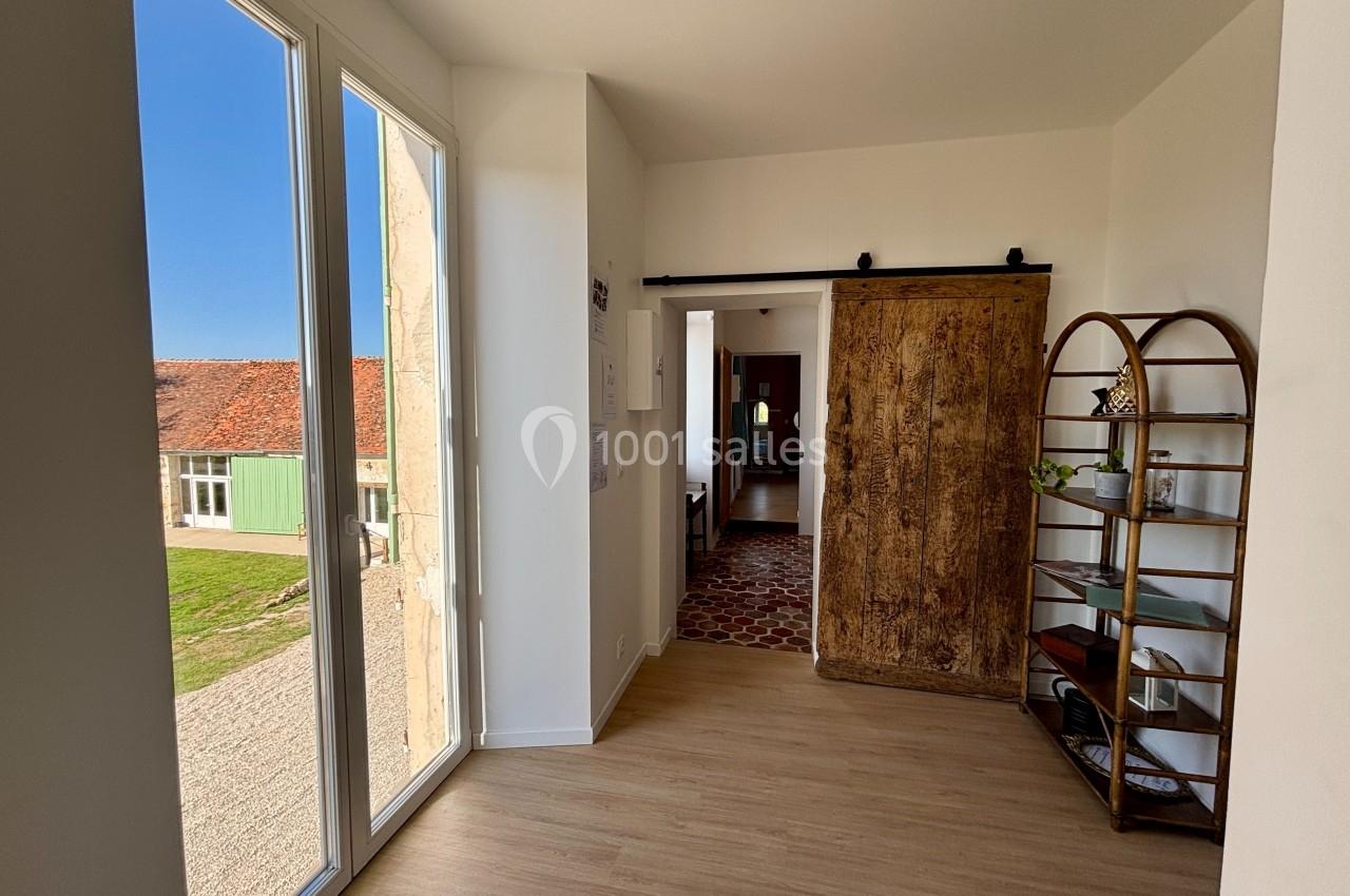 Entrée lumineuse avec porte coulissante en bois, étagère métallique et vue sur l'extérieur ensoleillé.