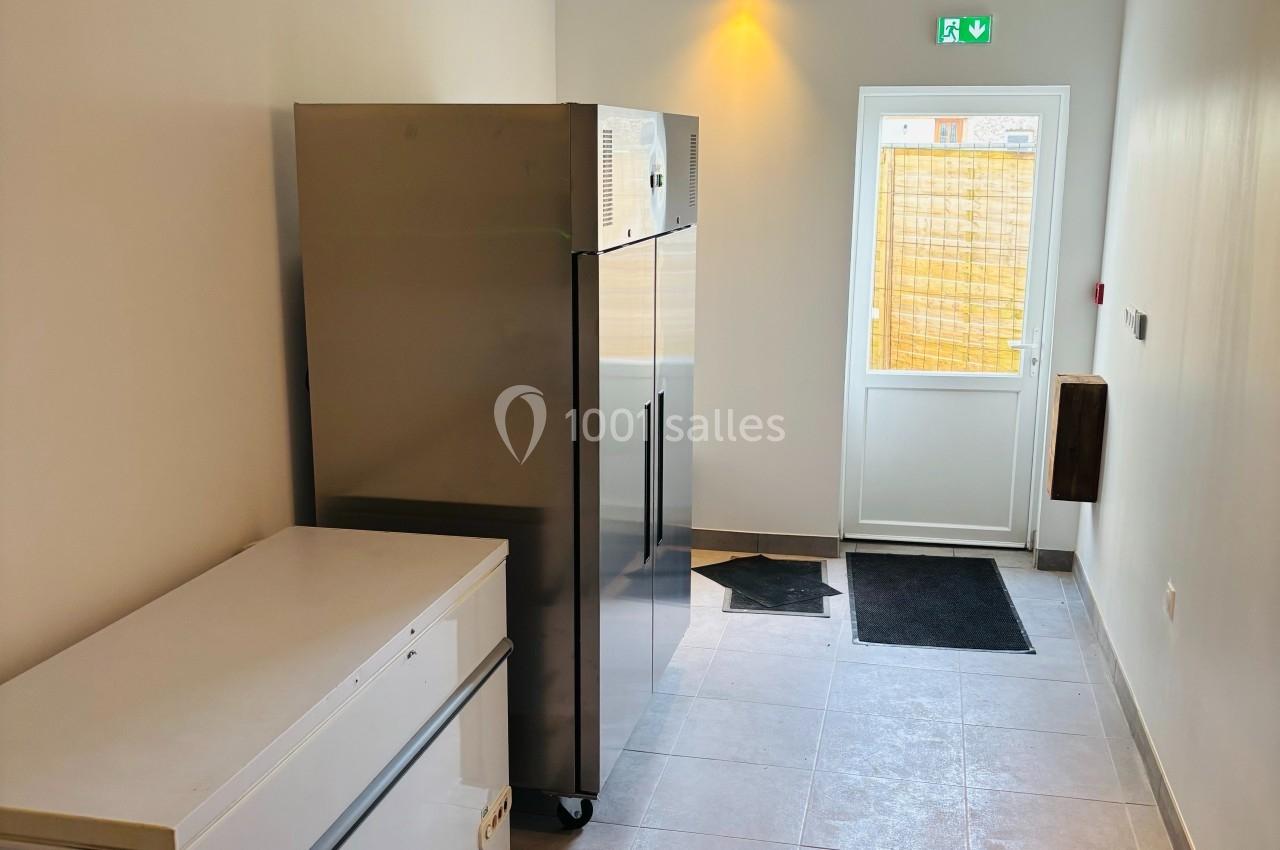 Couloir lumineux avec un congélateur, un réfrigérateur inox et une porte vitrée donnant sur l'extérieur.