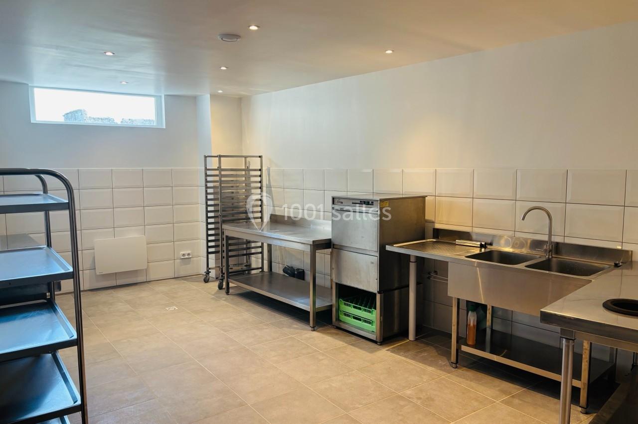 Cuisine professionnelle avec équipements en inox, étagères, évier, lave-vaisselle et carrelage mural blanc.