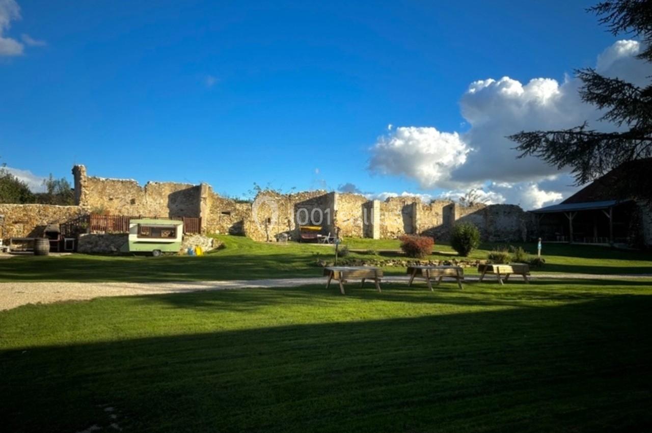 Ruines d'un ancien bâtiment en pierre entourées d'une pelouse verte, avec quelques bancs et un ciel dégagé.