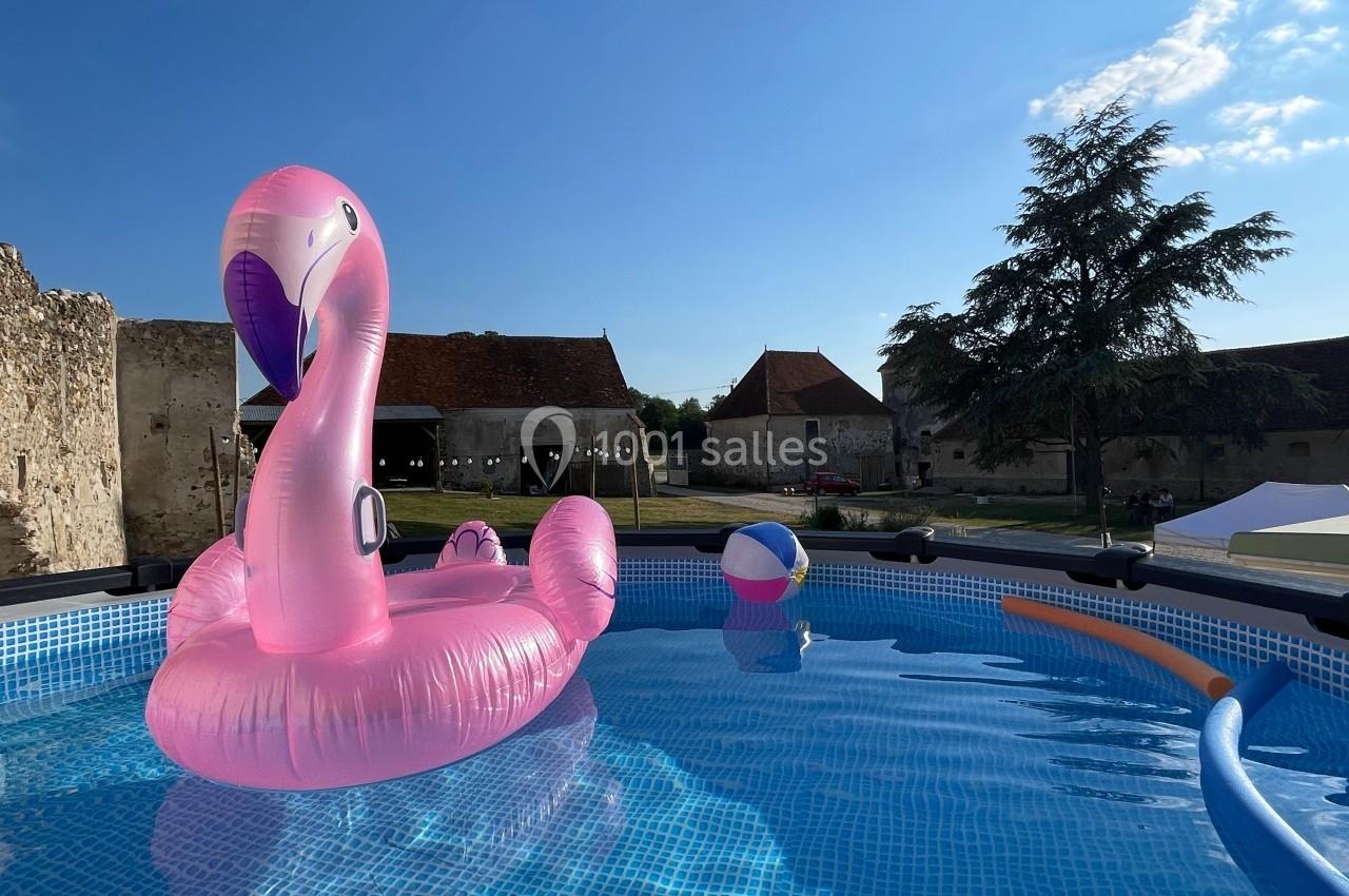 Piscine gonflable avec une bouée rose en forme de flamant rose et une balle colorée, sous un ciel bleu dégagé.