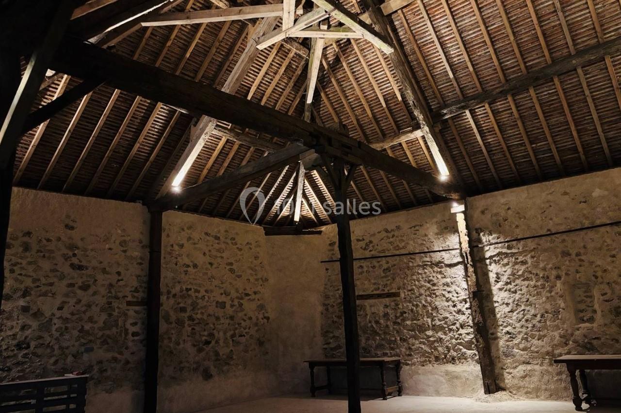 Charpente en bois apparente dans une pièce aux murs en pierre, éclairée par une lumière tamisée.