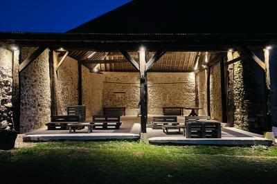 Miniature Le préau de nuit Ruines éclairées et bâtiment adjacent sous un ciel nocturne, avec un arbre illuminé et des bancs sur une pelouse.