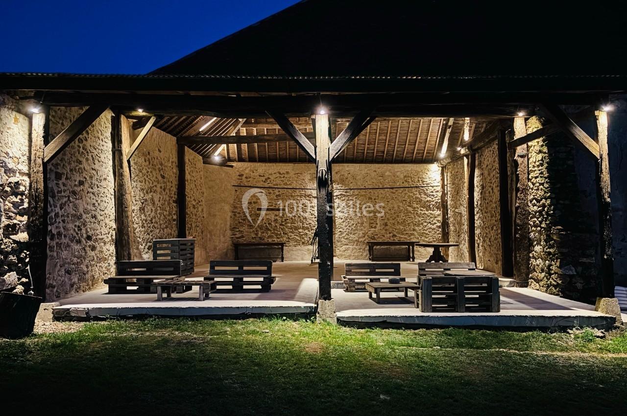Grange en pierre éclairée de nuit, aménagée avec des meubles en palettes sur un sol en béton.