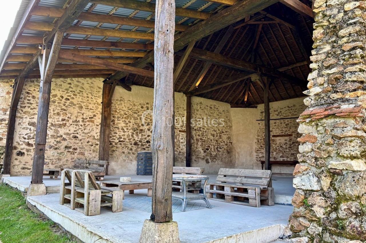Abri en pierre et bois avec toit en tôle, aménagé de bancs et tables en bois sur une dalle de béton.