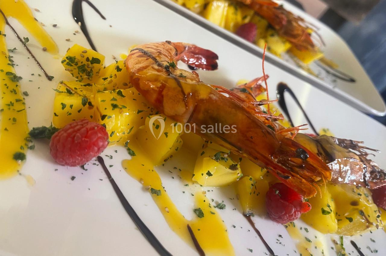 Assiette gastronomique avec crevettes grillées, morceaux de mangue, framboises et sauce décorative.