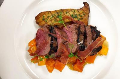 Assiettes composées de steaks grillés, purée, groseilles rouges, salade verte garnie de fleurs comestibles et sauce.