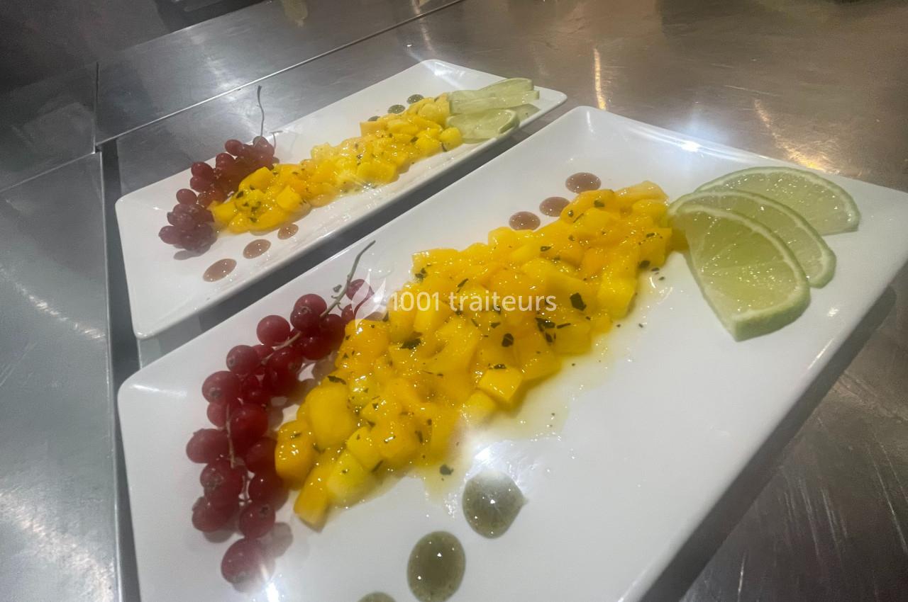 Assiettes de salade de mangue fraîche avec groseilles, tranches de citron vert et sauce, servies sur une table en inox.