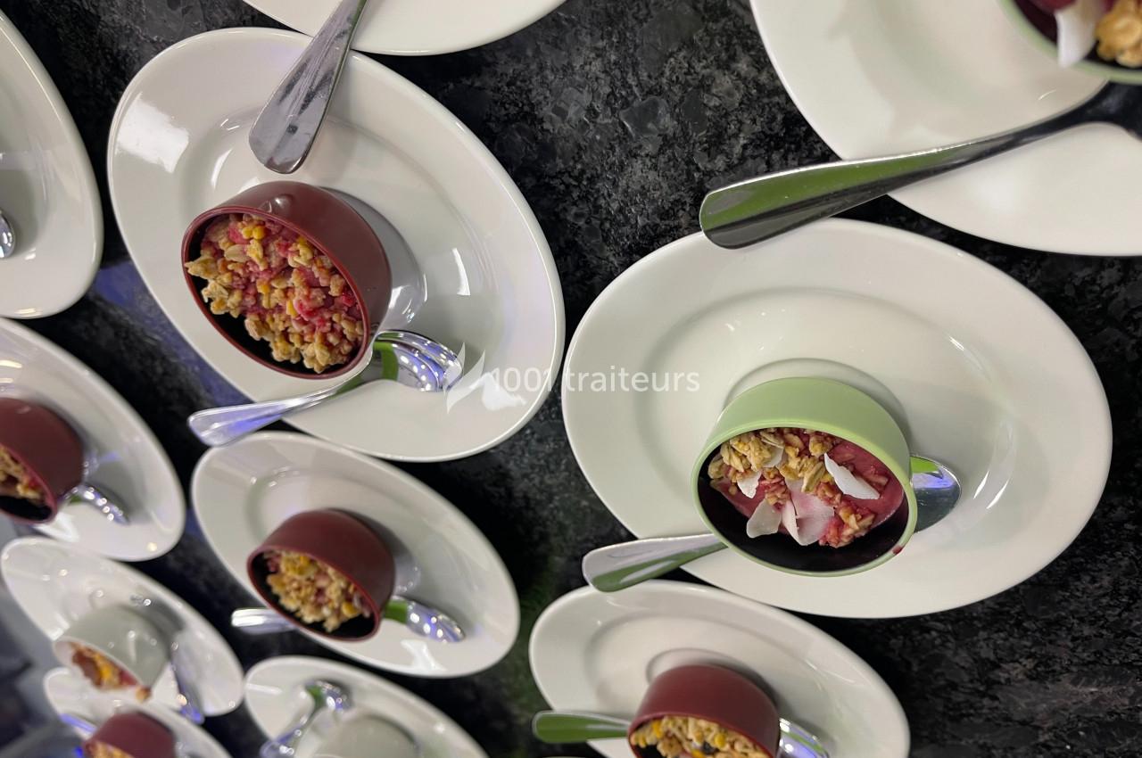 Des verrines de dessert avec fruits et crumble, servies sur des assiettes blanches avec des cuillères en métal.