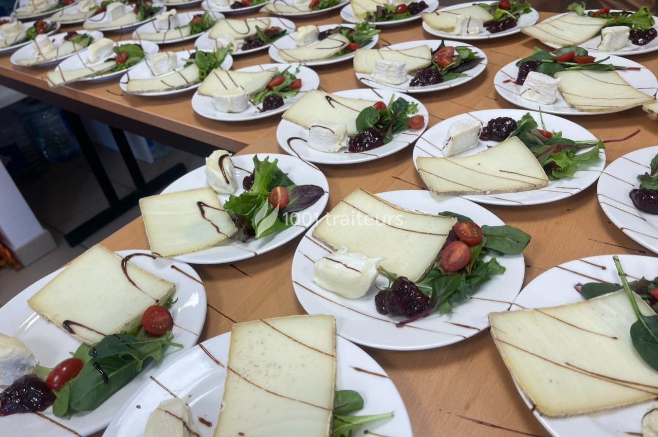 Assiettes de fromages variés accompagnées de salade, tomates cerises et confiture, disposées sur une table en bois.