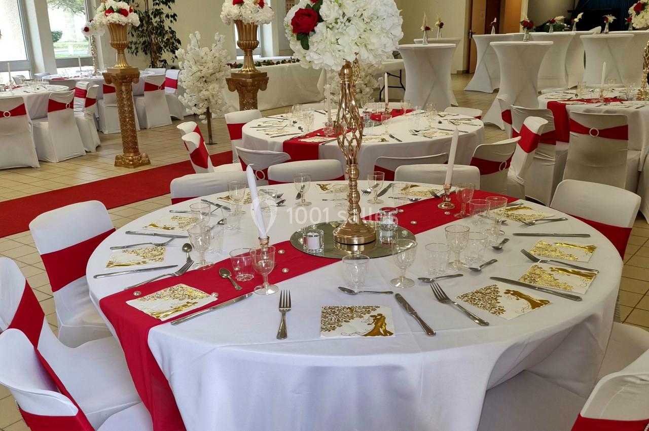 Salle de réception décorée avec des tables rondes ornées de nappes blanches, chemins de table rouges et centres de table…