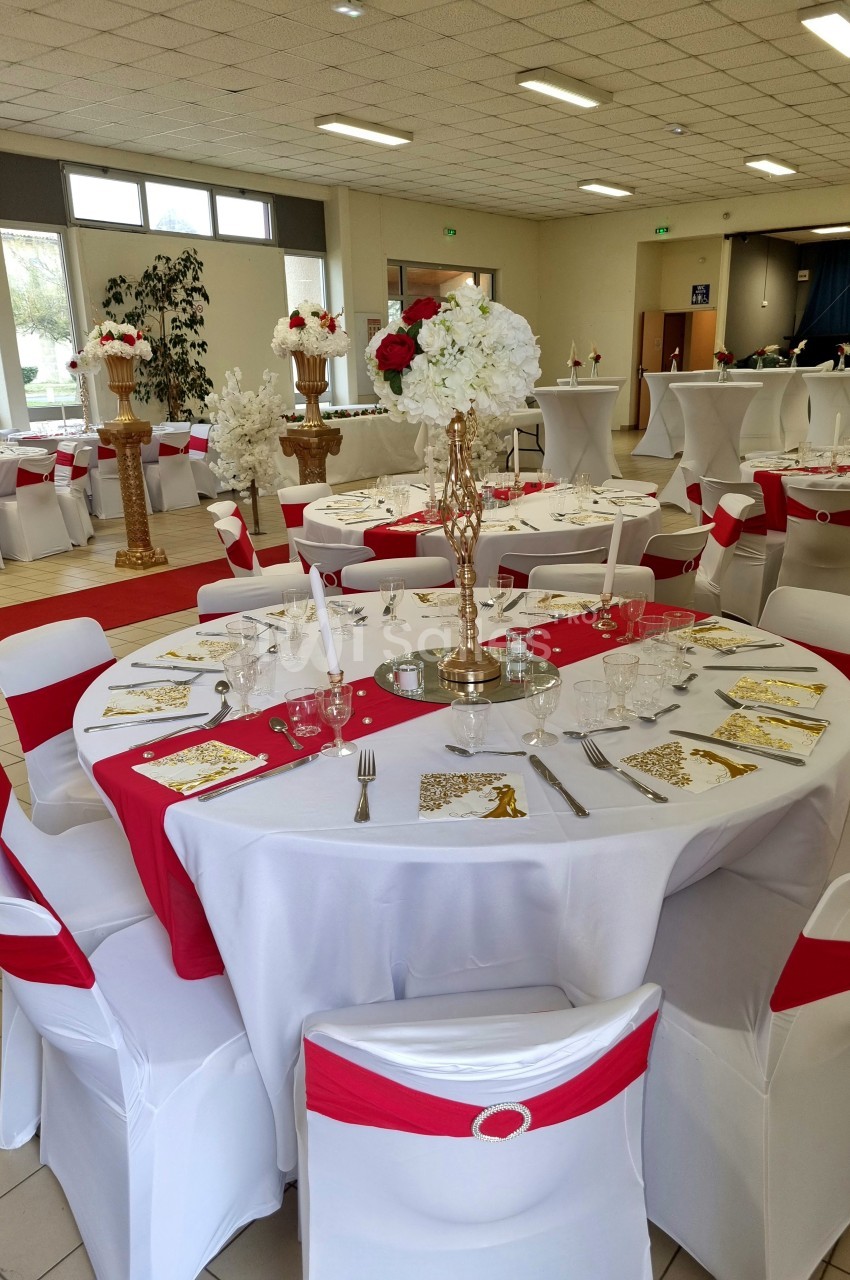 Salle de réception décorée avec des tables rondes ornées de nappes blanches, chemins de table rouges et centres de table…