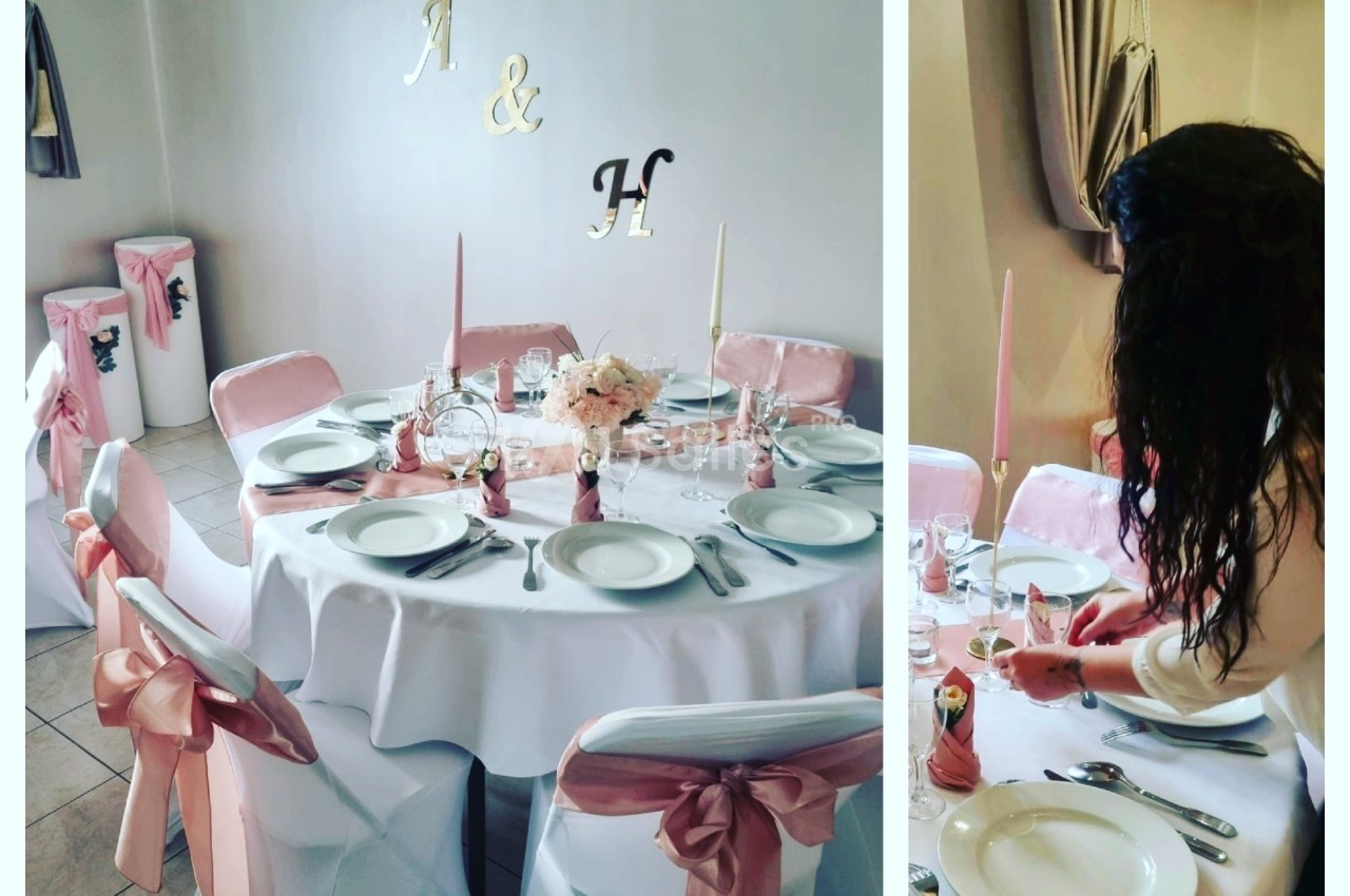 Table décorée pour un événement avec nappes blanches, rubans roses, bougies et une femme ajustant les détails.
