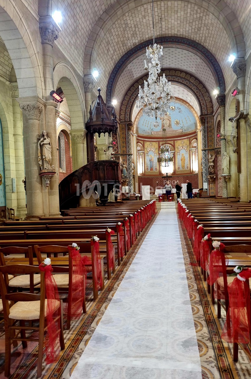 Intérieur d'une église décorée pour une cérémonie, avec des bancs ornés de rubans rouges et un autel en arrière-plan.
