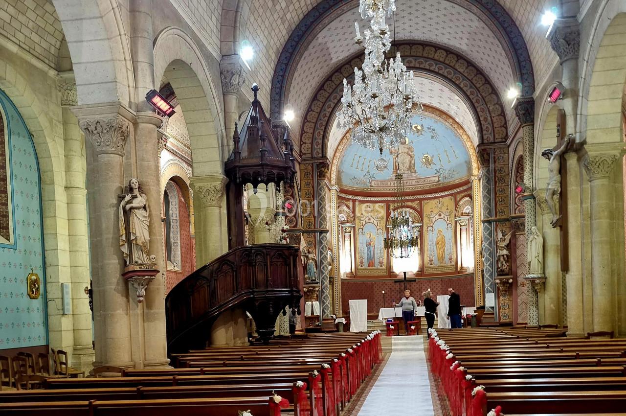 Intérieur d'une église avec bancs en bois, chaire sculptée, lustre central et fresques ornant le chœur.