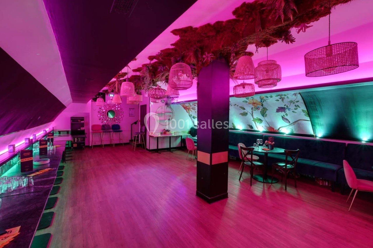 Salle moderne avec éclairage rose, tables et chaises, décorations suspendues et ambiance chaleureuse.