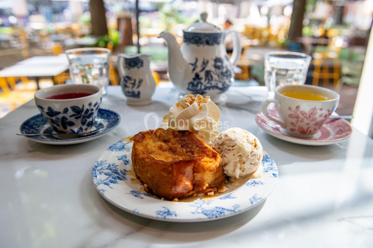 Assiette de pain perdu avec glace et chantilly, accompagnée de thé et café sur une table en terrasse.