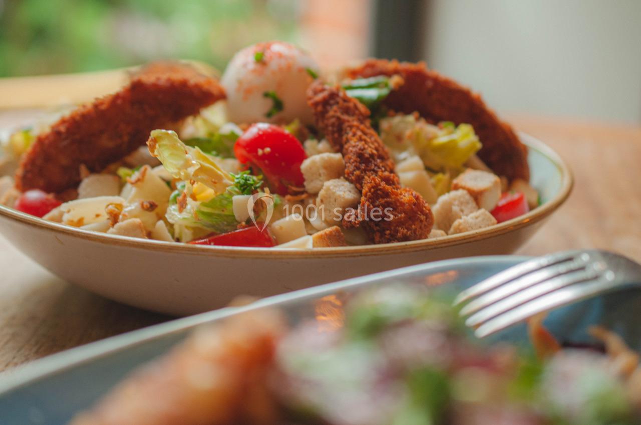 Salade composée avec morceaux de poulet pané, légumes frais, croûtons et œuf, servie dans un bol en céramique.