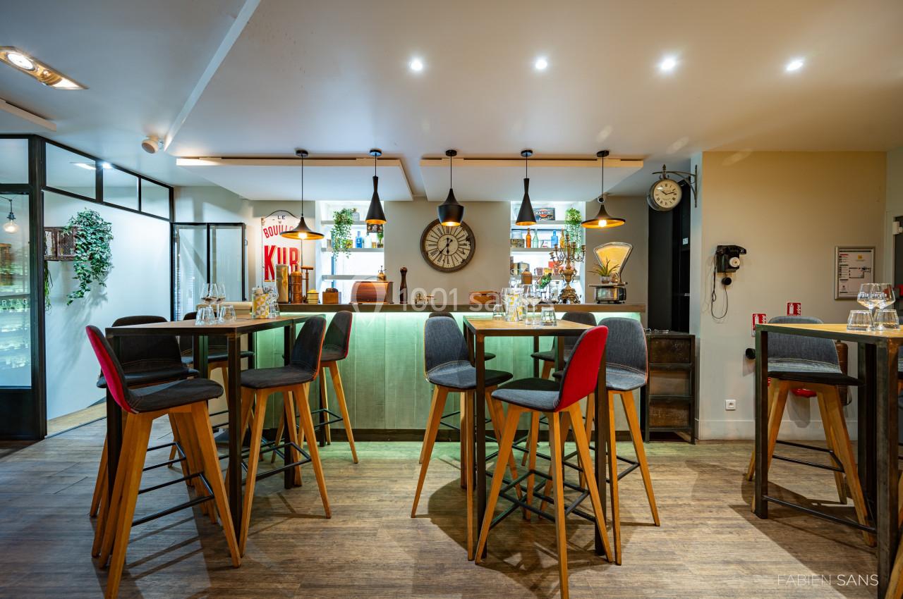 Salle de restaurant moderne avec tables hautes, chaises colorées, éclairage chaleureux et décorations murales.