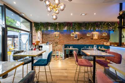 Salle de restaurant lumineuse avec banquettes bleues, chaises colorées, décor végétal et éclairage chaleureux.