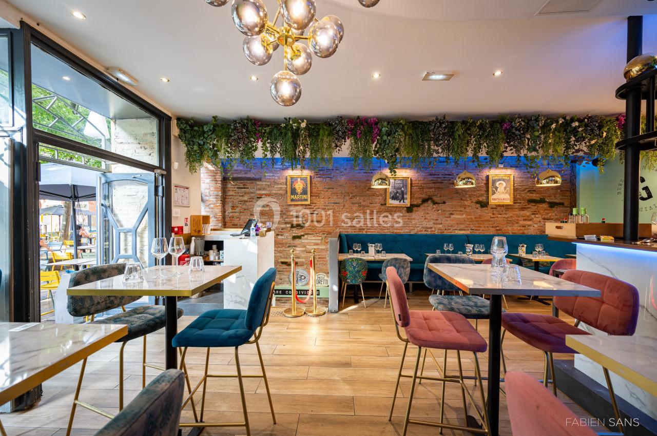 Intérieur d'un restaurant moderne avec tables, chaises colorées, mur en briques, plantes suspendues et éclairage design.