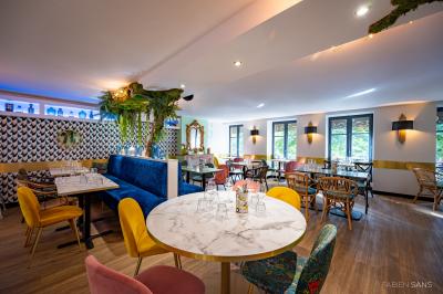 Salle de restaurant lumineuse avec banquettes bleues, chaises colorées, décor végétal et éclairage chaleureux.
