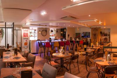 Salle de restaurant lumineuse avec banquettes bleues, chaises colorées, décor végétal et éclairage chaleureux.