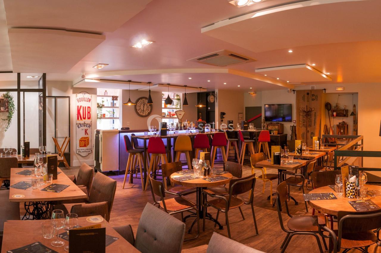 Intérieur d'un restaurant chaleureux avec tables dressées, bar coloré et décoration murale éclectique.