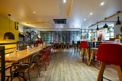 Salle de restaurant lumineuse avec banquettes bleues, chaises colorées, décor végétal et éclairage chaleureux.