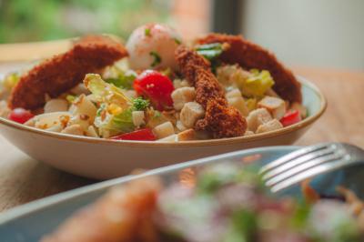 Salle de restaurant lumineuse avec banquettes bleues, chaises colorées, décor végétal et éclairage chaleureux.