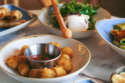 Salle de restaurant lumineuse avec banquettes bleues, chaises colorées, décor végétal et éclairage chaleureux.