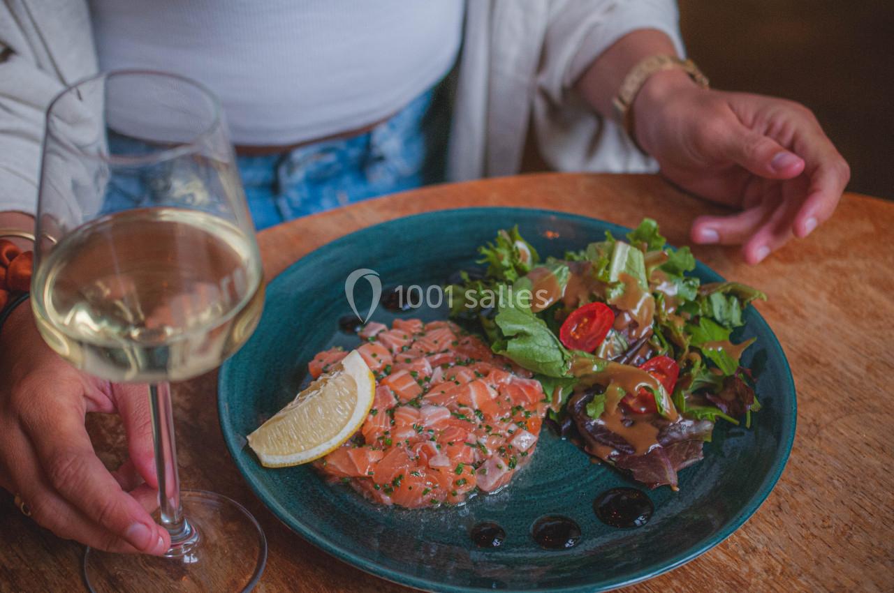 Assiette de tartare de saumon avec citron, salade verte et sauce, accompagnée d'un verre de vin blanc.