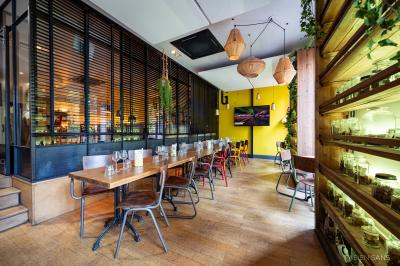 Salle de restaurant lumineuse avec banquettes bleues, chaises colorées, décor végétal et éclairage chaleureux.