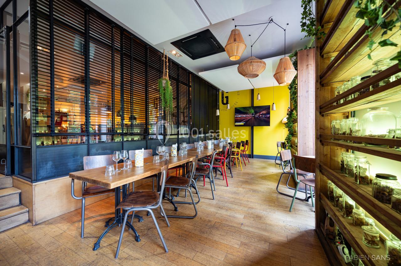 Salle de restaurant lumineuse avec tables en bois, chaises colorées, murs jaunes et étagères décorées de bocaux.