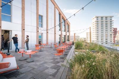 Bâtiment moderne en briques avec de grandes fenêtres, entouré de végétation et de parasols jaunes au premier plan.