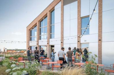 Bâtiment moderne en briques avec de grandes fenêtres, entouré de végétation et de parasols jaunes au premier plan.