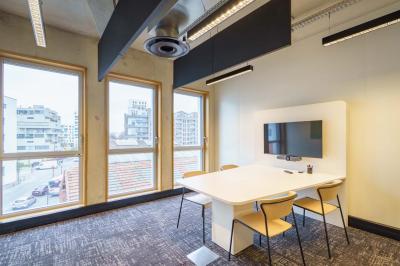 Bâtiment moderne en briques avec de grandes fenêtres, entouré de végétation et de parasols jaunes au premier plan.