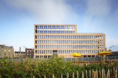Bâtiment moderne en briques avec de grandes fenêtres, entouré de végétation et de parasols jaunes au premier plan.