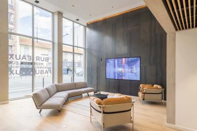 Bâtiment moderne en briques avec de grandes fenêtres, entouré de végétation et de parasols jaunes au premier plan.