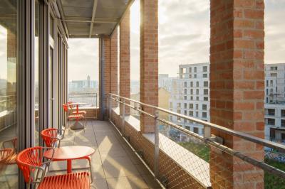 Bâtiment moderne en briques avec de grandes fenêtres, entouré de végétation et de parasols jaunes au premier plan.