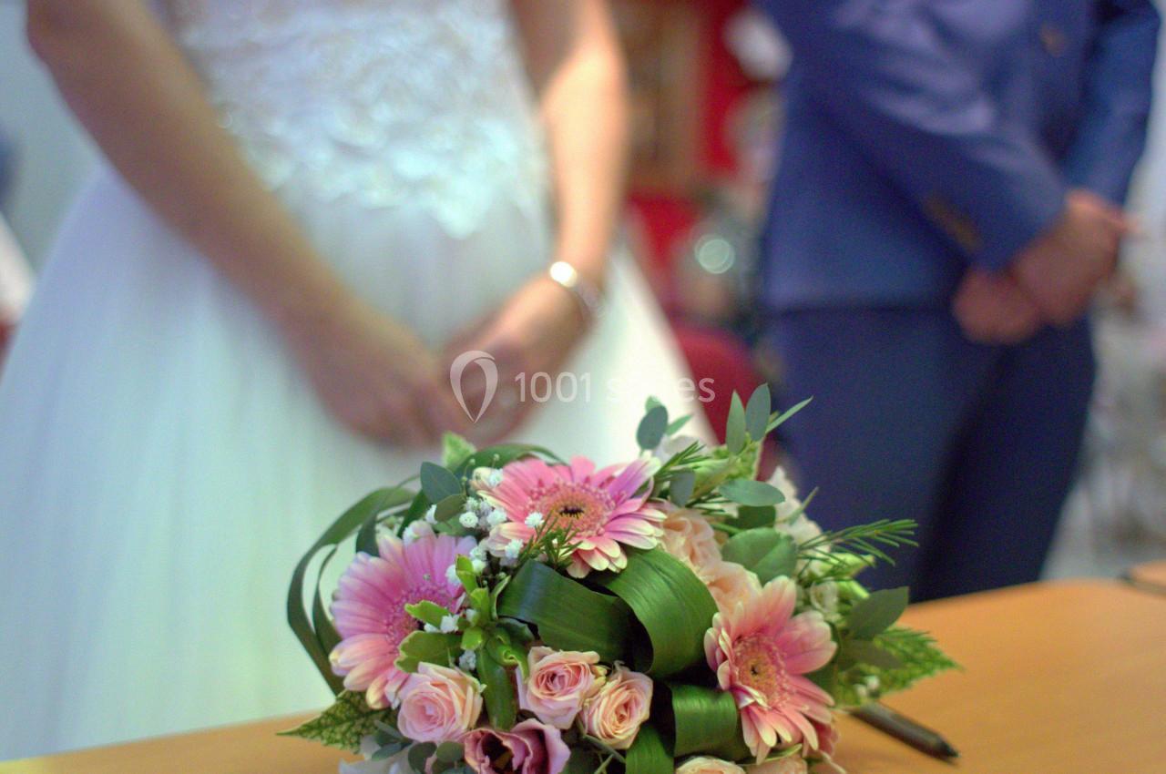 Un bouquet de fleurs posé sur une table devant une mariée en robe blanche et un homme en costume bleu.