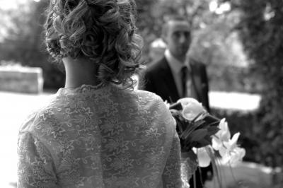 Miniature Cédric Chapelon Photographe #5 Femme en robe de mariée blanche tenant un bouquet de fleurs blanches et décorations bleues, en extérieur sur pelouse.
