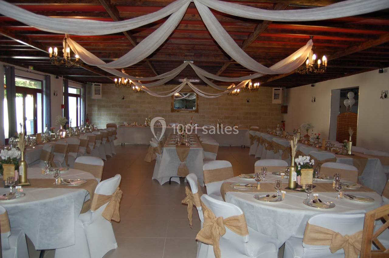 Salle de réception décorée avec des nappes blanches, des rubans beiges et des drapés suspendus au plafond.