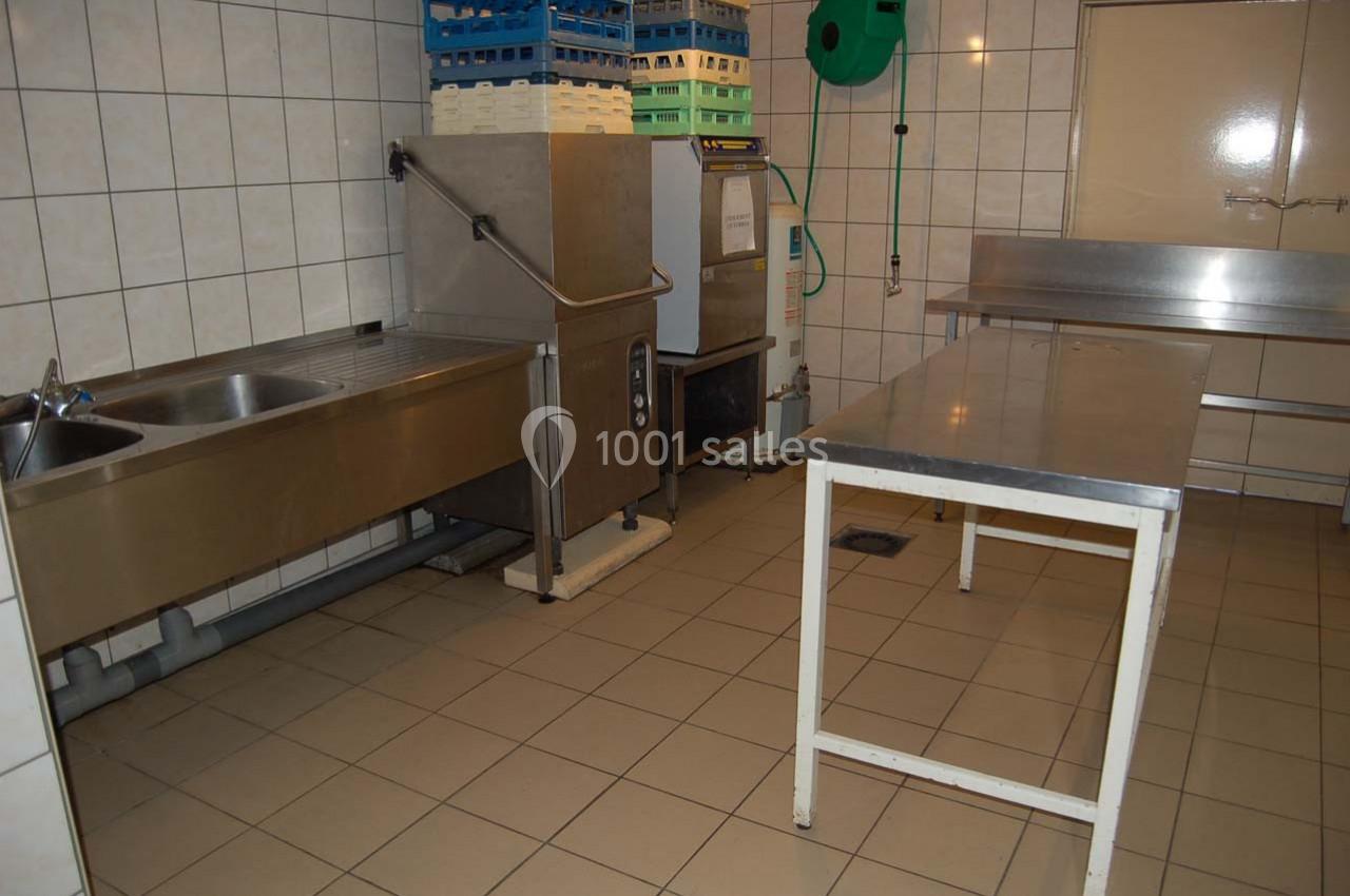 Cuisine professionnelle avec évier inox, lave-vaisselle industriel, table en métal et étagères de rangement.