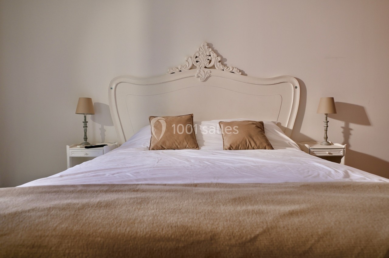 Lit double avec tête de lit sculptée, draps blancs, coussins beiges et lampes de chevet assorties dans une chambre sobre.