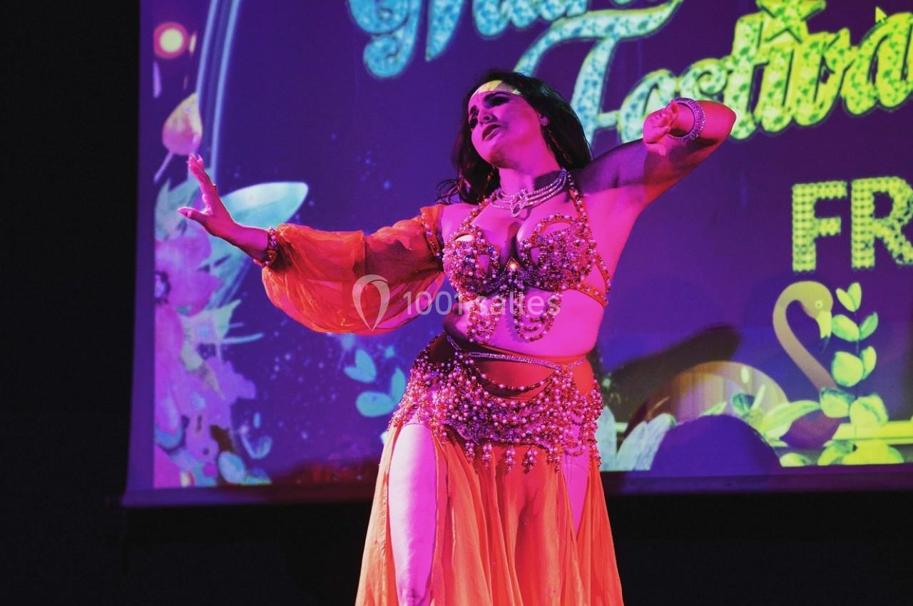 Danseuse en costume oriental coloré exécutant une performance sur une scène éclairée avec un fond visuel vibrant.